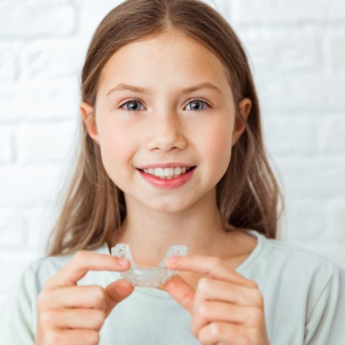 Smiling child girl with perfect and healthy teeth using removable braces or aligner for straightening and whitening teeth. Orthodontic treatment for correction of bite